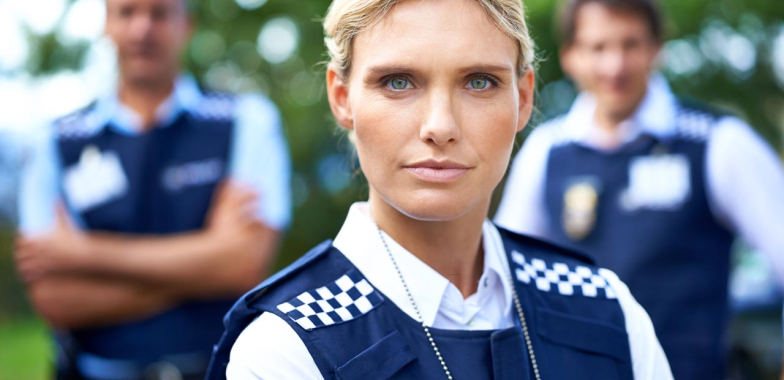 Female police officer looking at camera with two male officers behind blurred