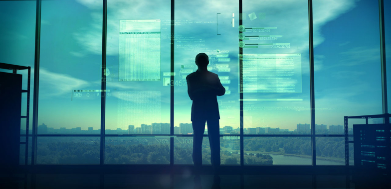 Man standing looking out a window at a sunset over a city 