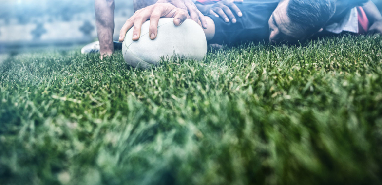 Rugby players in a scrum on the ground with one player's hand on the ball