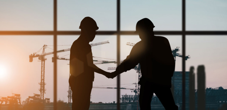 Two construction workers shaking hands with cranes in the distance