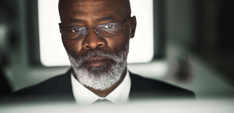 A man in glasses looking at a screen in the direction of the camera