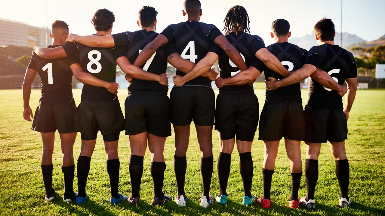 Rugby players in a line with arms round each other facing away from camera