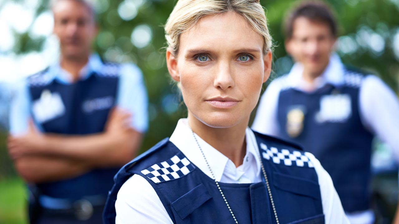 Female police officer looking at camera with two male officers behind blurred