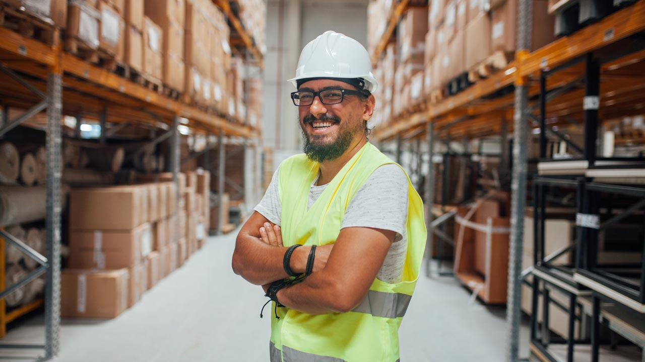 Man in hard hat and high vis vest in a warehouse smiling at camera