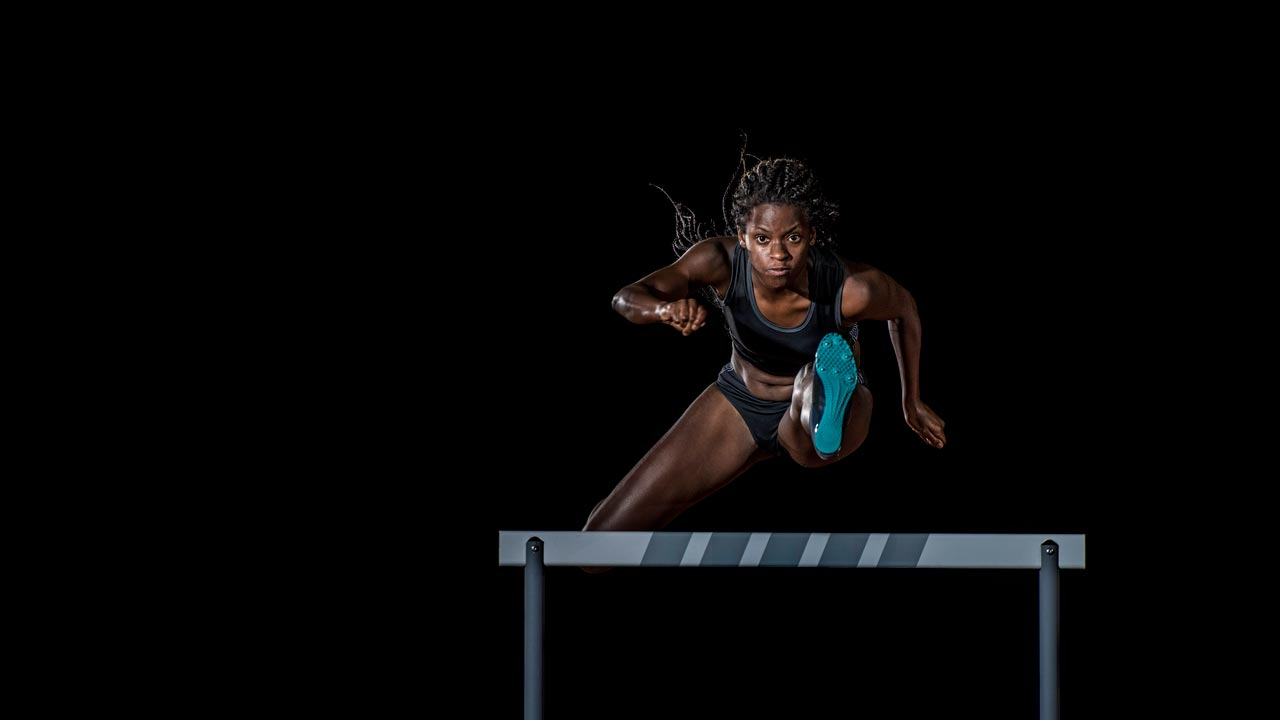 Female athlete running towards camera jumping a hurdle