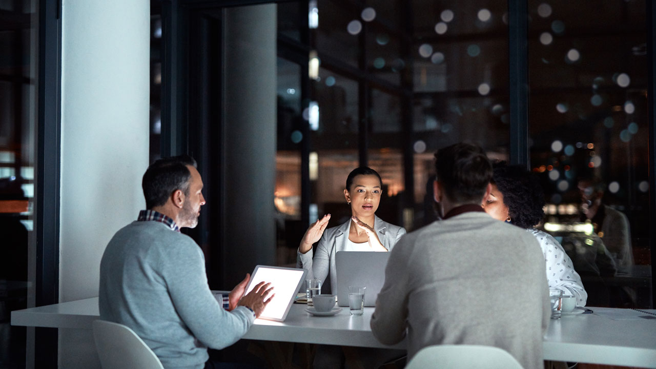 Four workers sitting around a table with laptops having a meeting in the evening