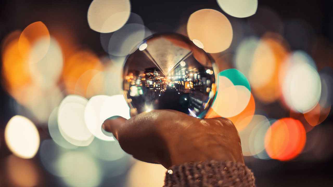A hand with a crystal ball in it's palm with blurred lights in the background