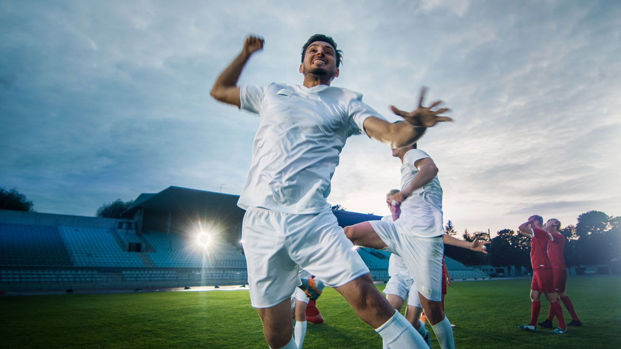Soccer players walking on a pitch with one punching the air in celebration